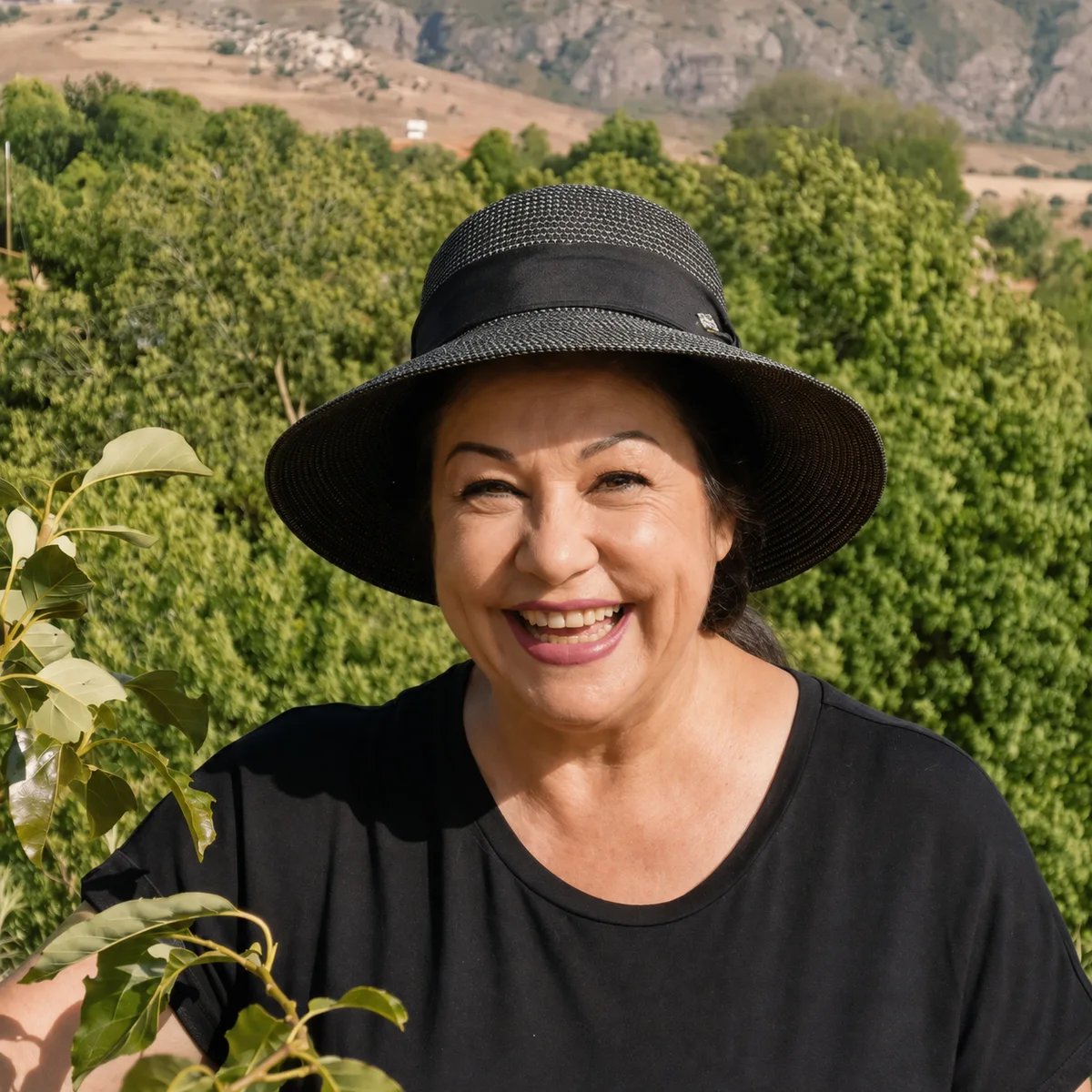 Sabine Kuhn mit Sonnenhut lacht herzlich in die Kamera, hinter ihr grüne Hügel
