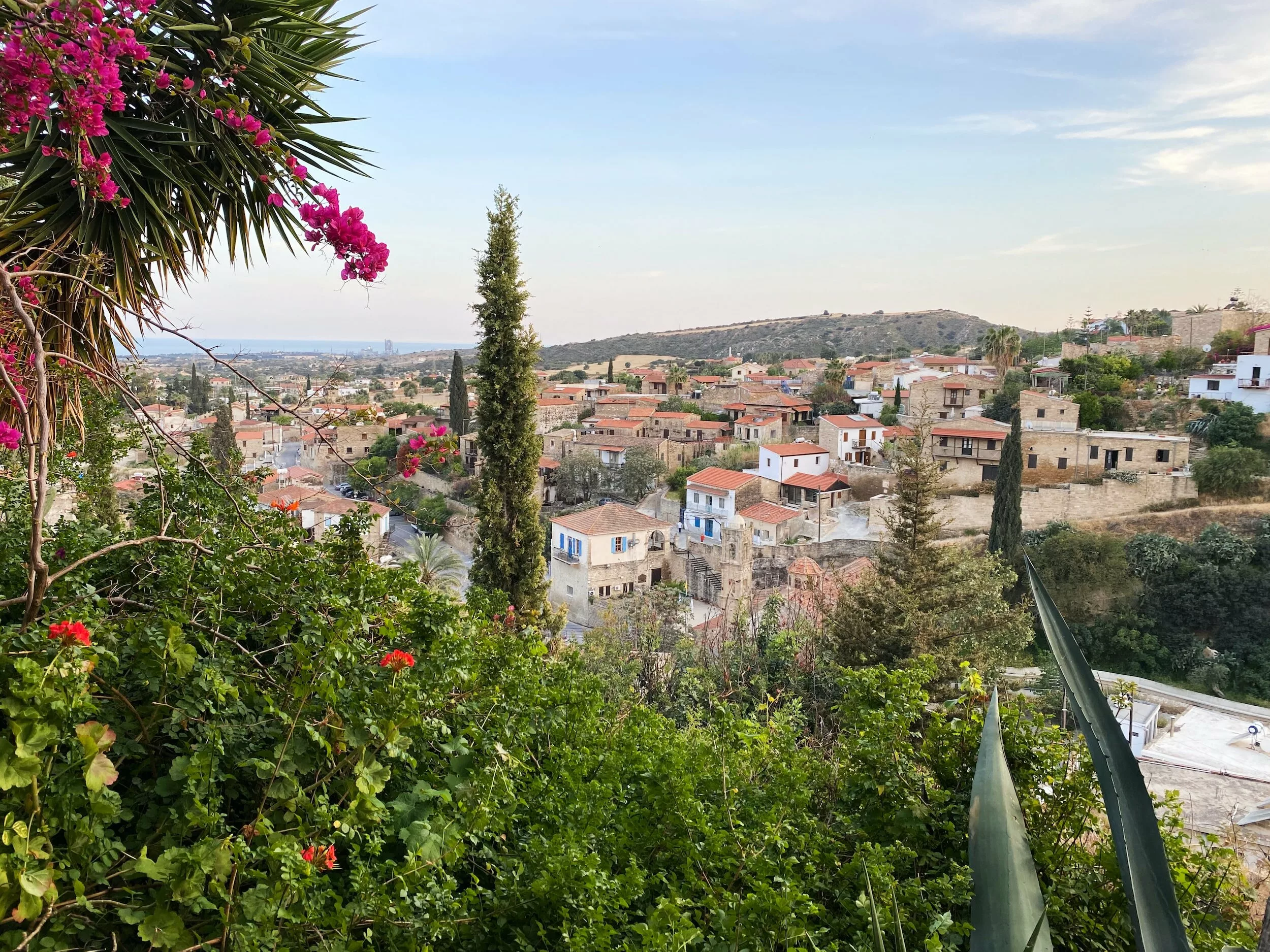 Blick über Sabines Dorf auf Zypern: Steinhäuser mit roten Dächern, Zypressen, blühende Bougainvillea, am Horizont das Meer